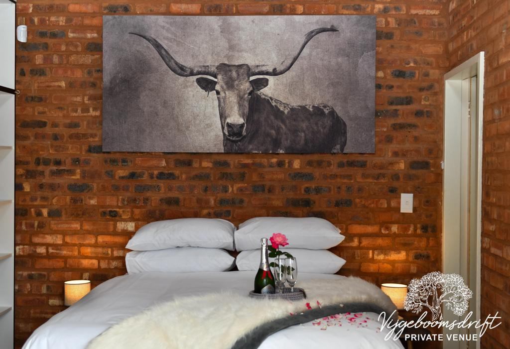 Guest room with white linen and a framed Nguni bull print on the brick wall
